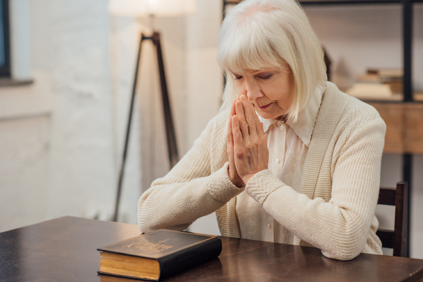 concentrata donna anziana seduta a pregare davanti alla santa bibbia a casa
 - Foto, immagini