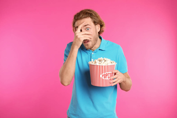 Emotional man with popcorn during cinema show on color background - Foto, immagini