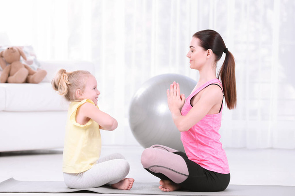 Sportive woman doing fitness exercises with daughter at home - Foto, Imagen