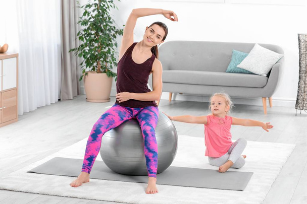 Sportive woman doing fitness exercises with daughter at home - Фото, зображення