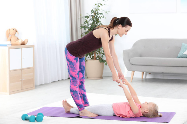 Sportive woman doing fitness exercises with daughter at home - Foto, Bild