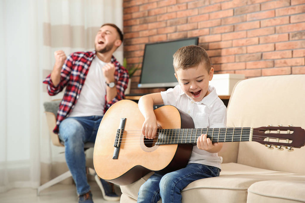 Father and son playing guitar and singing at home - Fotó, kép