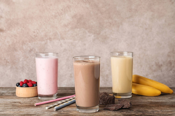 Glasses with different protein shakes and ingredients on table against color background - Photo, Image