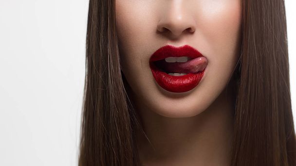 Close-up of sexy female lips with tongue. Clean skin and a clear lip contour are outlined with a fashionable red lipstick. White teeth and the beauty of a smile for stamotologii, spa or cosmetology - Foto, afbeelding