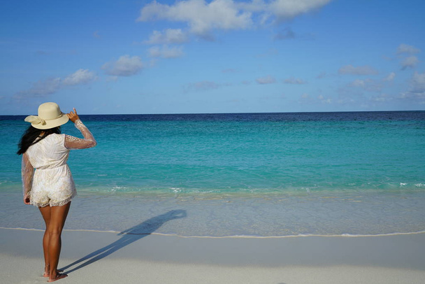 вид ззаду жінки в капелюсі позує на піщаному пляжі біля моря
 - Фото, зображення