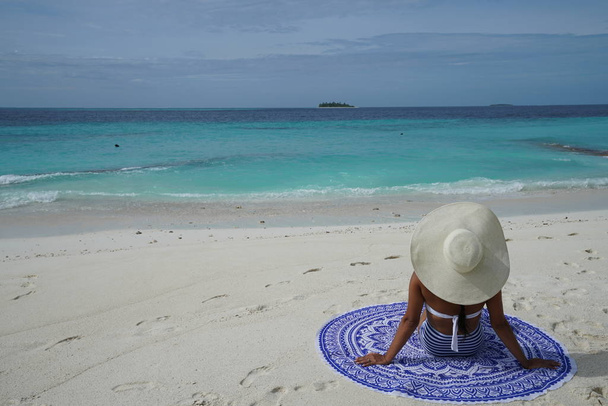 nézet hátulról nő ül a homokos strand kalap viselése - Fotó, kép