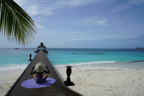 Frau mit Hut sitzt auf Holzsteg in tropischer Szenerie - Foto, Bild