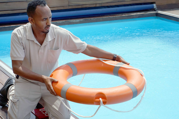 救命浮輪プールである救助者の手。ホテルの労働者は、溺死のプールにライフラインをスローします。沈みゆく人の救い。プールで人生はリング。赤い救命浮輪うきわ. - 写真・画像