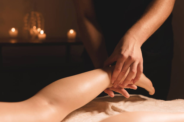 Close-up of male hands doing calf massage of female legs in a dark room with candles in the background. Cosmetology and spa treatments - Φωτογραφία, εικόνα