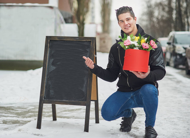 мужчина держит красную подарочную коробку с красивым букетом цветущих розовых, желтых и белых тюльпанов и белых хризантем с зелеными листьями, символ романтического момента, женский день и День Святого Валентина
 - Фото, изображение