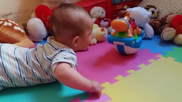 χαριτωμένο μωρό αγόρι στην κοιλιά που προσπαθούν να φθάσουν παιχνίδια, πολύχρωμα playmat - Πλάνα, βίντεο