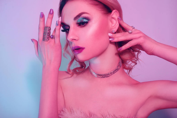 Beautiful woman in a necklace, earrings and ring. Model in jewelry, diamonds. Fashion neon portrait of young beautiful girl with jewelry. Blond girl with cerly hair and red lips. Perfect make-up.  - Фото, изображение