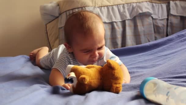 sleepy newborn baby boy crawling on his tummy, reaching for soft toy puppy and milk bottle - Imágenes, Vídeo