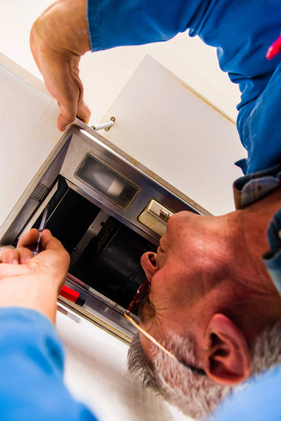 Зрілий ремонтник фіксує установку кухонної вентиляційної витяжки викруткою
 - Фото, зображення