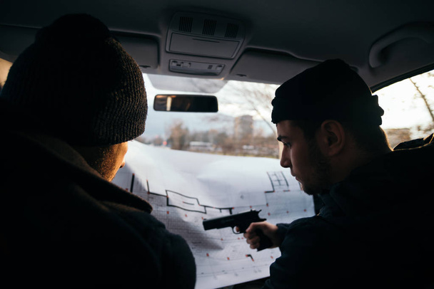 Два грабителя планируют и указывают на план (карту) своей цели, держа в руках оружие. - Фото, изображение
