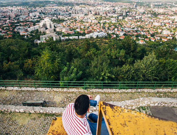 Mann sitzt auf Eisenkonstruktion und betrachtet friedlich das Stadtpanorama - Foto, Bild