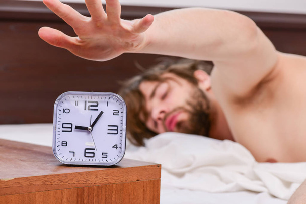 Veselý mladý muž se probouzí po ranním spánku. Pohledný muž používá hodiny v posteli, když se ráno probudí. Muži v posteli. - Fotografie, Obrázek