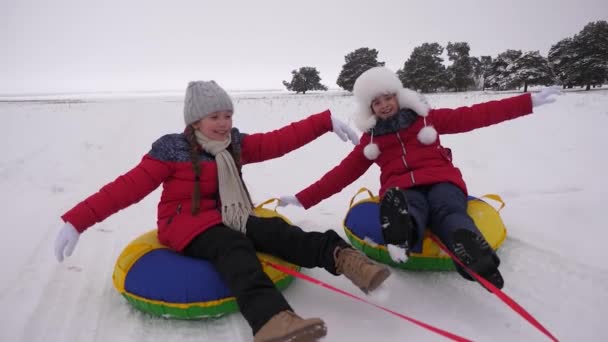 children ride through snow in winter on an inflatable snow tube. girls relax in winter park for the Christmas holidays. Slow motion - Footage, Video