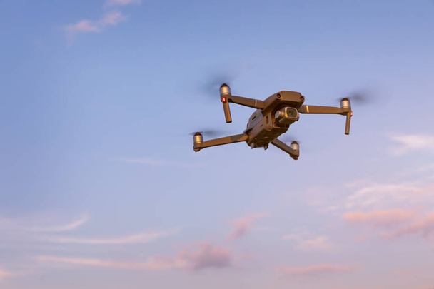 Drone πετάει πάνω από το τοπίο. UAV κηφήνας copter που φέρουν με ψηφιακή φωτογραφική μηχανή. Drone πετώντας πάνω από το κεφάλι στο θολό μπλε του ουρανού. Quad copter που πετούν πάνω από το πεδίο. - Φωτογραφία, εικόνα