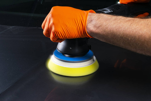 Car polish wax worker hands applying protective tape before polishing. Buffing and polishing car. Car detailing. Man holds a polisher in the hand and polishes the car. Tools for polishing - 写真・画像