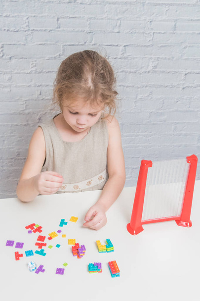 child, a girl in a dress playing logic designer, on a white wall background - Foto, afbeelding