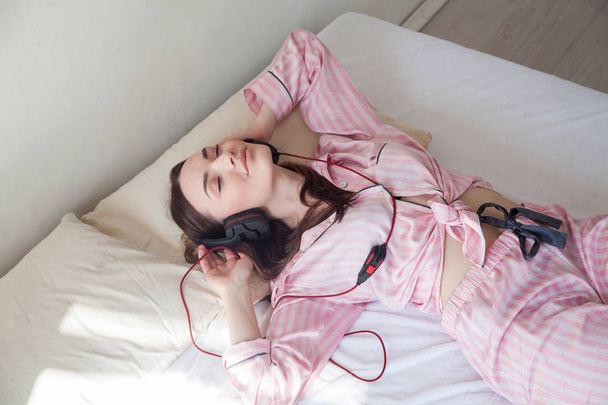 mulher em rosa Pajamas ouvir música em fones de ouvido dançando na cama
 - Foto, Imagem