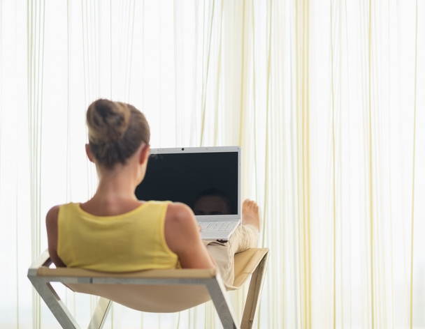 Young woman sitting on modern chair with laptop. rear view - Photo, Image