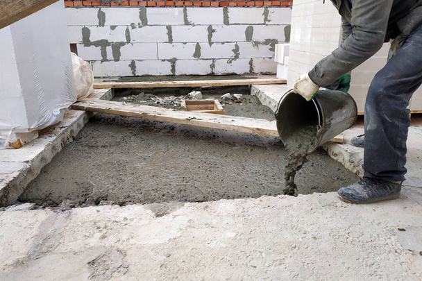 Hilfsarbeiter schüttet flüssigen Zementmörtel aus einem Eimer auf den Boden zwischen den Etagen des Hauses - Foto, Bild