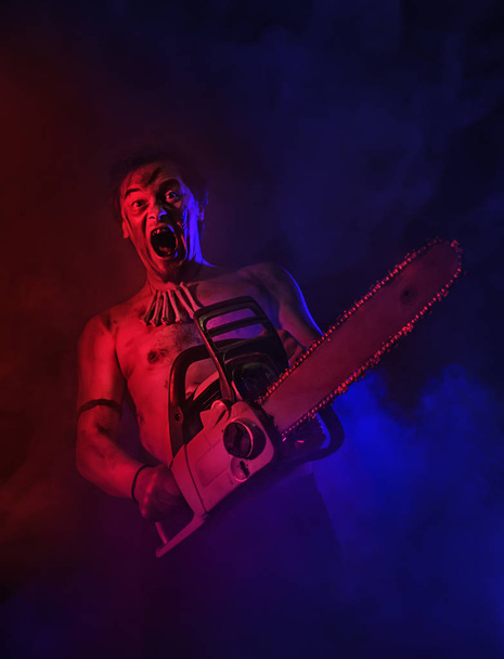 Terrible homme avec tronçonneuse criant dans le brouillard rouge et bleu. Scène Halloween
 - Photo, image