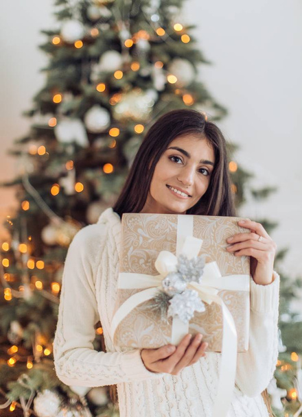 Beautiful woman with gift near Christmas tree posing at home  - Foto, imagen