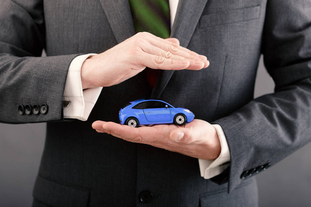 Businessman holding a small car in his hand. The idea of protection  - Foto, Imagem