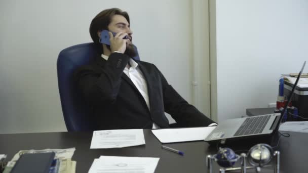 Magabiztos és sikeres üzletember beszél telefonon, és ül egy széken. Üzleti tárgyalások. - Felvétel, videó