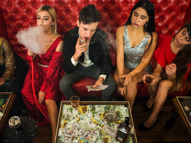 Skupina mladých multietnické přátel relaxační v shisha baru club v bohatých interiérů. Muž s doutníkem počítání peněz v klubu - Fotografie, Obrázek