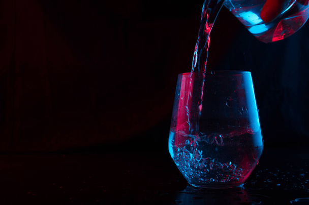 Water highlighted in blue and red splashing into a glass goblet on a black background - Photo, image