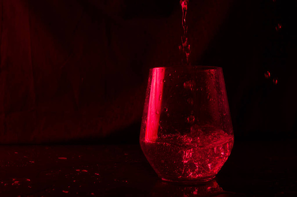 Water highlighted in blue and red splashing into a glass goblet on a black background - Foto, immagini