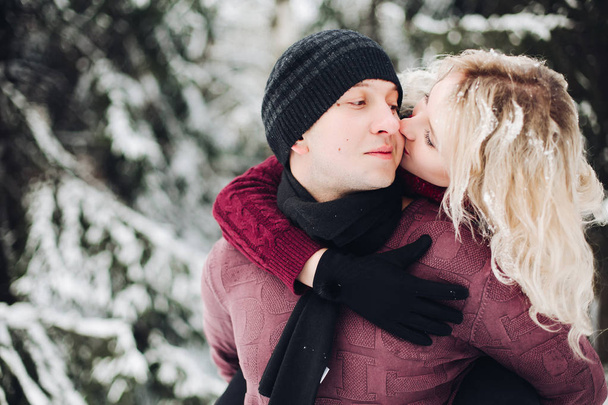 Couple in red sweaters having fun among snowing forest and kissing. - Photo, Image