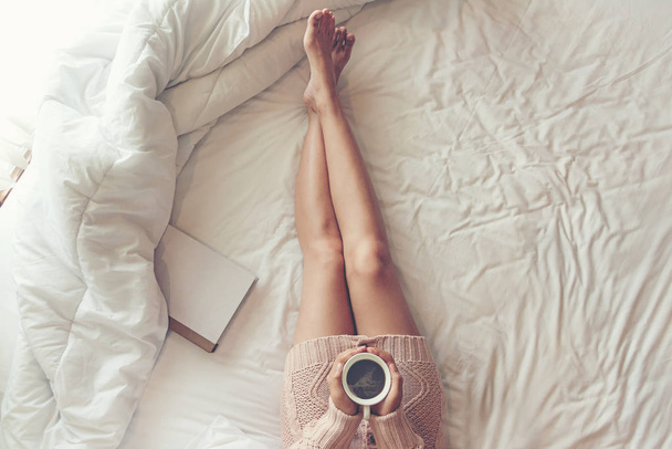 Close up legs women on white bed. Women reading book and drinking coffee in morning relax mood in winter season. Lifestyle Concept - Foto, Bild