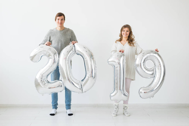 Новий 2019 рік ідея - смішний молодий чоловік і жінка тримають срібні кольорові цифри на білому тлі
 - Фото, зображення