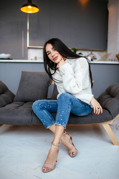 Beautiful girl in a white jacket and jeans is resting on the sofa at home. portrait, scandinavian style - Fotoğraf, Görsel