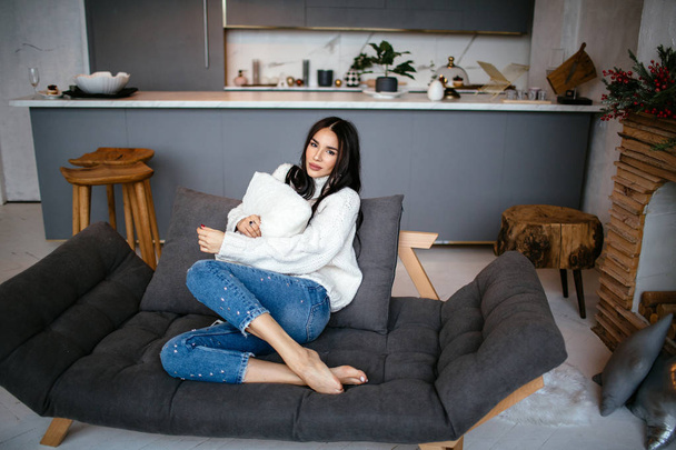 Beautiful girl in a white jacket and jeans is resting on the sofa at home. portrait, scandinavian style - Photo, image