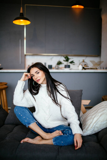 Beautiful girl in a white jacket and jeans is resting on the sofa at home. portrait, scandinavian style - Foto, Bild