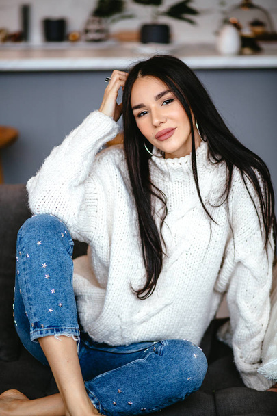 Beautiful girl in a white jacket and jeans is resting on the sofa at home. portrait, scandinavian style - Foto, afbeelding