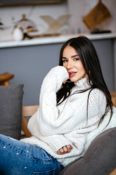 Beautiful girl in a white jacket and jeans is resting on the sofa at home. portrait, scandinavian style - Φωτογραφία, εικόνα