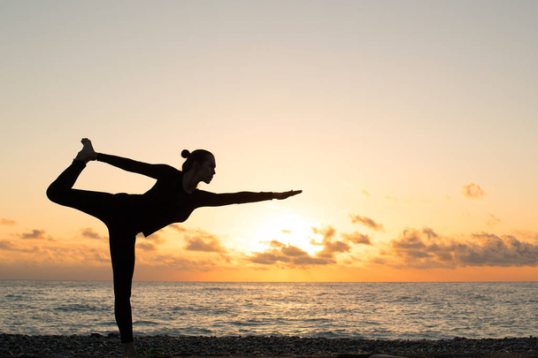 einsame Silhouette einer Frau, die bei Sonnenuntergang Yoga am Strand praktiziert - Foto, Bild