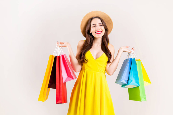 Spring summer season sale concept. Attractive young woman with long brunette hair, wearing sexy yellow dress, holding many different blank shopping bags over white background. Copy space, close up. - Foto, imagen