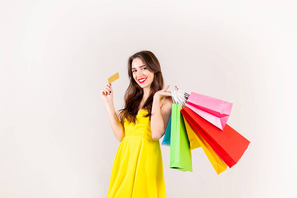 Spring summer season sale concept. Attractive young woman with long brunette hair, wearing sexy yellow dress, holding many different blank shopping bags over white background. Copy space, close up. - Fotografie, Obrázek