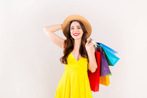 Spring summer season sale concept. Attractive young woman with long brunette hair, wearing sexy yellow dress, holding many different blank shopping bags over white background. Copy space, close up. - Zdjęcie, obraz