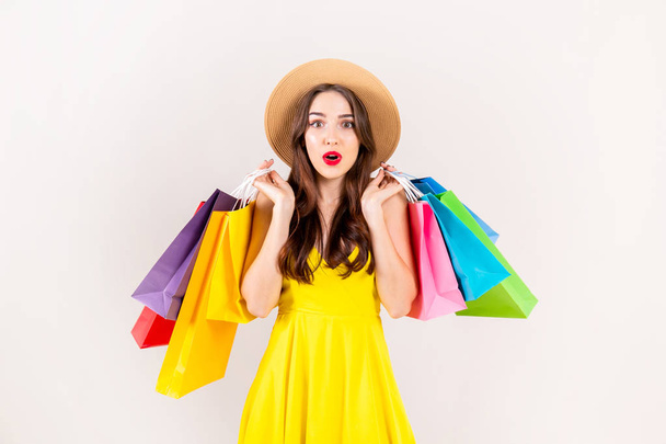 Spring summer season sale concept. Attractive young woman with long brunette hair, wearing sexy yellow dress, holding many different blank shopping bags over white background. Copy space, close up. - 写真・画像
