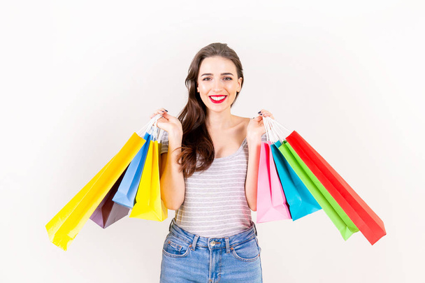 Spring summer season sale concept. Attractive young woman with long brunette hair, wearing slim fit casual shirt, holding many different blank shopping bags over white background. Copy space, close up - Fotó, kép