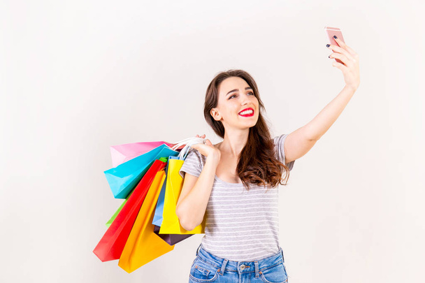 Spring summer season sale concept. Attractive young woman with long brunette hair, wearing slim fit casual shirt, holding many different blank shopping bags over white background. Copy space, close up - Foto, Imagen
